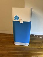 Front view of Blue by Blueair Pure 121 air purifier showing white top and bottom sections with blue body and circular front knob.