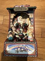 Front view of Christmas music box showing Santa Claus and two smaller figures, decorated with music hall background and a painted castle scene on base.