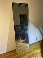 Full-length frameless mirror leaning against wall, showing visible smudges and marks on reflective surface.