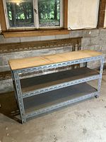 Shelving unit shown front angled view, highlighting plywood shelves and metal frame in a concrete and block wall setting.