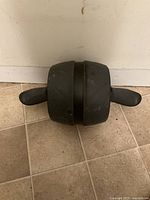 Top view of the Harbinger ab roller on tiled floor showing black central wheel with black handles extending out on each side.