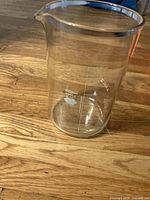 Full view of the large graduated glass beaker on wooden floor, showing cylindrical shape and spout.