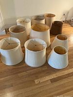 Top view of 11 yellowed vintage lamp shades arranged on wooden floor showing various sizes and shapes