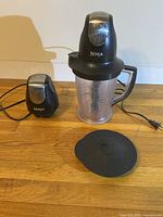 Ninja blender with two motor units, clear 48 oz container with handle, detachable blade and black flat lid, all placed on wooden surface