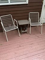 Pair of off-white metal grid design folding chairs with small brown plastic folding table between them on wood floor.
