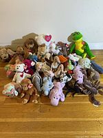 Overall group of 28 various Ty Beanie Babies stuffed animals on wooden floor including bears, frogs, dogs, monkeys, snails, birds, and others