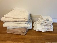 Photo showing folded stack of 6 bath towels and 9 hand towels of various neutral colors like white, off-white, beige.