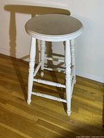 Full view of the white wooden stool showing turned legs and round seat with visible wear.