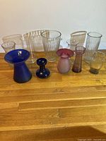 All 10 vases grouped on wooden floor showing variety of clear, blue, and colored glass pieces