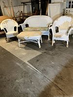 Wicker furniture set including two armchairs, one loveseat, and one ottoman in a worn white finish with floral cushions.