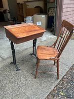 Side view of vintage wooden school desk with black metal adjustable legs and hinged top, next to matching wooden chair.