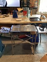 Full view of stainless steel BBQ grill with foldable stand and cooking grate on top.