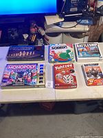 Six board games shown on table including Chess-Checkers-Backgammon set, Monopoly Empire, Sorry!, Battleship original and travel edition, and Yahtzee.