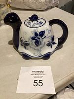 Porcelain teapot shaped like a turtle showing front and side with floral and butterfly blue patterns.
