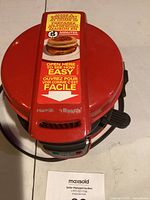 Closed red Hamilton Beach sandwich cooker with instructions and branding visible on top.
