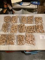 Overview image of 15 sealed plastic bags filled with many natural cork wine bottle stoppers on a white table surface.