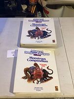 Two Advanced Dungeons & Dragons Monstrous Compendium Volume One books, one loose and one in box, on a table.