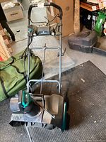 Front view of electric snowblower showing green and black body with chute and wheels.