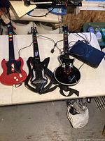 Three guitar controllers and PlayStation 2 console laid out on a table with cables visible.