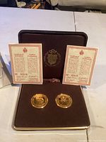 Two gold plated coins displayed in a burgundy case with two certificates of authenticity.