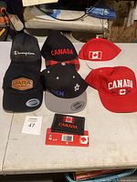 Group photo of five baseball caps and one wallet, showcasing various Canada-themed designs and logos.