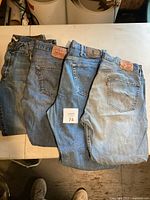 Four pairs of men's jeans laid out folded on table, showing variety of blue washes and leather patches with brand labels.