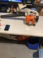 Side view of Stihl BG 56 C leaf blower layed on table with blower tube and phone beside for scale.