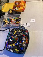 Overview photo showing three containers filled with assorted LEGO pieces including a yellow compartment box, a clear plastic bin, and a blue soft-sided container