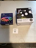 Both product boxes placed side-by-side on a table: Smart RGB LED Strip Light and Solar Living Bulb String Lights.