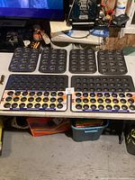 Six nonstick black metal mini muffin pans arranged on a table with two original packaging inserts visible, four pans have 12 cavities, two have 24 cavities.
