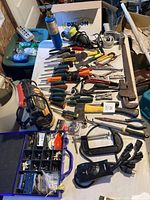Photo showing a layout of assorted hand tools on a table, screwdrivers, pliers, wrenches, a hammer, and an EverStart battery charger.