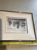 Front view of framed black and white print showing four wolves walking in a snowy forest scene. The frame is metallic with a cream mat.
