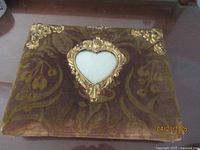 Top view of antique photo album with velvet floral cover, gold accents, and heart-shaped mirror frame.