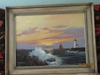Full front view of framed oil on canvas painting, showing the entire coastal scene with waves, lighthouse, sailboat and sunset. Frame is gold tone with a subtle decorative border.