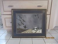 Full frontal image of the framed watercolor farm scene with birds in flight, resting against kitchen cabinetry.