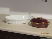 View of both casserole dishes on countertop, white Wedgwood dish on left, brown Hull Pottery dish with lid on right