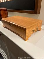 Closed wooden jewelry chest made from light-colored wood with decorative feet and metal handles on the sides.