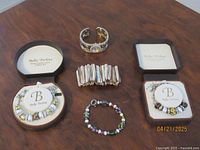 Two Bella Perlina bracelets in original boxes, shell expandable bracelet, and a multicolored beaded bracelet laid out on wood surface.