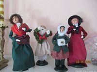 Photo showing all four Victorian Byers' Choice caroler figurines together: Mrs. Cratchit, Victorian adult male, Victorian teen female with muff, and Victorian adult female in red dress.