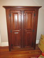 Front view of wooden cabinet with doors closed showing paneled design and hardware