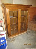 Front angle view of the vintage wooden cabinet with closed glass doors, showing overall condition and design.