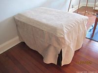 Closed convertible bed with beige cloth cover skirt on wooden floor near wall.