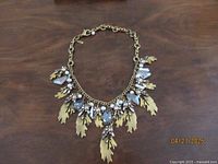 Full view of the gold-tone necklace laid out flat showing chain and leaf pendants with crystals and pearls.