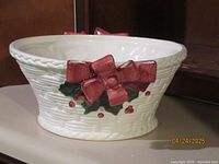 Front view of oval white ceramic bowl with basket weave texture, red painted bows and red floral details.