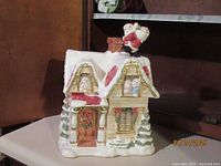 Front and side view of hand-painted Victorian house cookie jar with Santa on chimney, snow, wreaths, and holiday decorations.