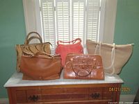 Five handbags arrayed on a marble table showing variety of sizes, colors and materials