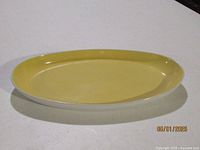 Oval yellow dish with smooth bright yellow glossy interior and white exterior shown from top view on white surface.