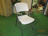 Single white Lifetime folding chair with contoured seat and back visible with metal frame on green floor