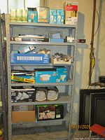Full view of metal shelving with multiple types of lightbulbs and lighting items stacked across 5 shelves, including large blue boxes and boxed fixtures.