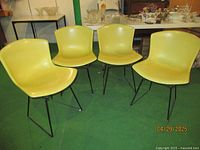 Four yellow chairs arranged in a row on green floor under table